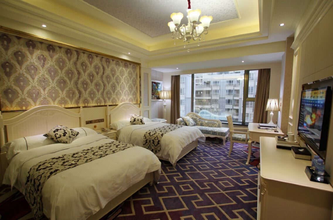 Een hotelkamer met twee bedden, een bureau, een televisie en een groot raam met uitzicht op gebouwen.