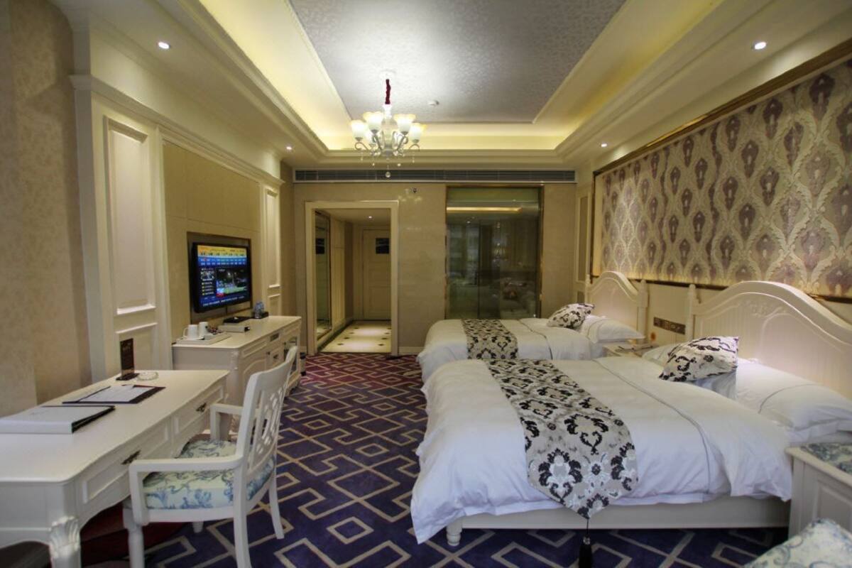 Une chambre d’hôtel avec un bureau, deux lits, une télévision et un papier peint à motifs.