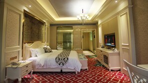 A hotel room with a large bed, a television, a desk, and a mirror. - Jin Long Wan Hao Hotel (Wuzhou)