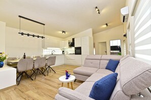 Ein modernes Wohnzimmer mit Sofa, Essbereich, Küche und Fernseher.