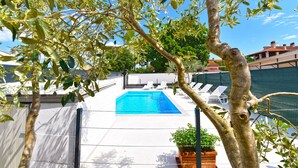 A swimming pool with white lounge chairs, surrounded by trees and a fence.