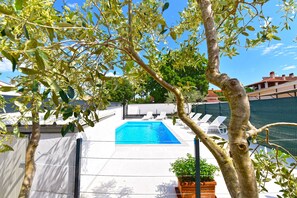 A swimming pool with white lounge chairs, surrounded by trees and a fence.