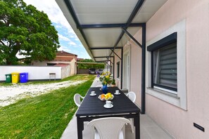 An outdoor patio with a table set for four, surrounded by white chairs, a covered area, and a view of a residential street.