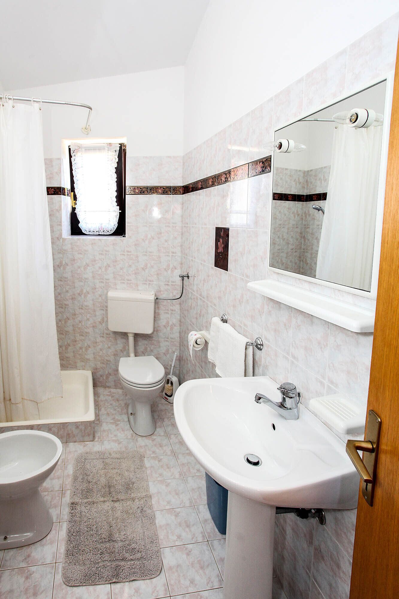 A bathroom with a toilet, bidet, sink, and a shower area.