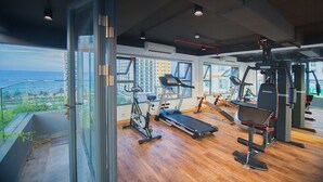 Un gimnasio moderno con varios equipos de ejercicio, ventanas amplias y vistas a la ciudad.