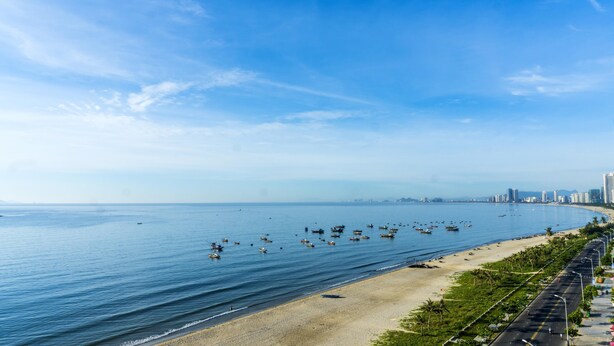 Un paisaje urbano costero con una playa extensa, numerosos barcos y un cielo despejado.