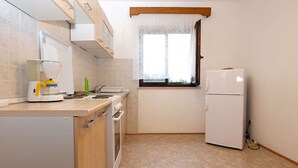 Pieni, käytännöllinen keittiö, jossa on kahvinkeitin, pesuallas, ikkuna verholla ja jääkaappi.