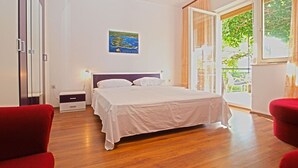 A bedroom with a large bed, a nightstand, a red chair, and a window with a view of greenery. - House 1214/11158 (Istria - Banjole), 400m from the beach (Banjole)