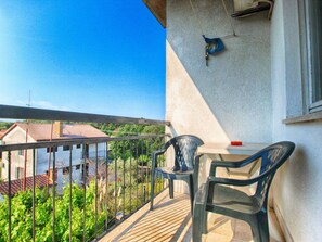 Un balcon donnant sur des maisons, une table avec des chaises et un climatiseur fixé au mur.