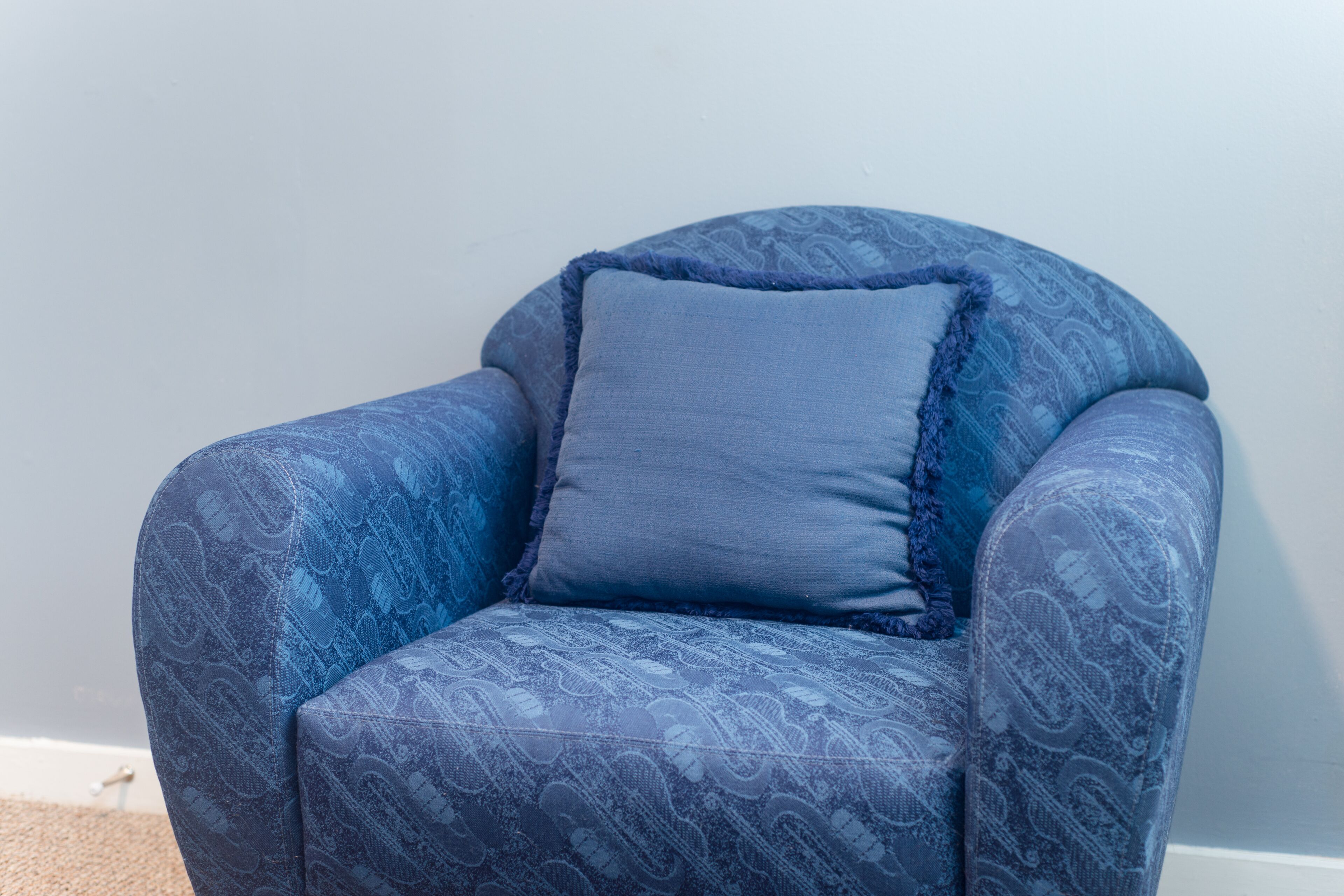 Una poltrona blu con rivestimento a fantasia e cuscino blu uniforme, su uno sfondo neutro.