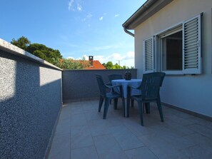 A patio with a table and chairs, a window with shutters, and a view of a building with a red roof. - Apartment 1215/11159 (Istria - Premantura), 500m from the beach (Premantura)