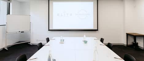 A conference room with a long table, chairs, a projector screen, and a whiteboard.