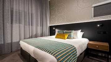 Une chambre d’hôtel moderne avec un grand lit, une table de chevet en bois et un mur orné d’un motif.