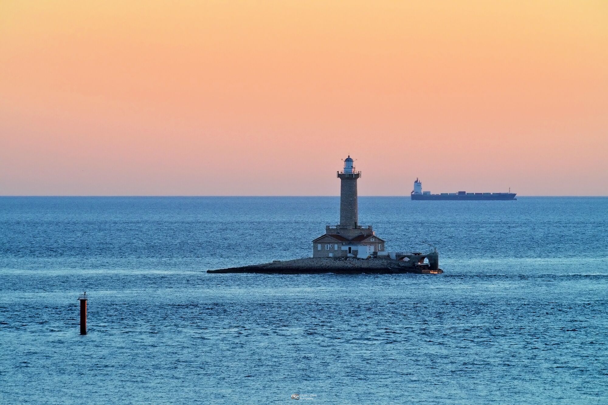A lighthouse on a pier with a cargo ship in the background.