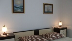 Une chambre avec deux lits, chacun étant équipé d’un oreiller et d’une table de chevet avec une lampe. Deux tableaux encadrés ornent le mur.