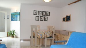 Un salon comprenant un coin repas, un canapé bleu, une table avec des chaises et des tableaux encadrés accrochés au mur.