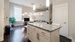 A modern kitchen with a granite countertop, white cabinets, and a built-in island. There is a ceiling fan, pendant lights, and a potted plant. - Modern & Stylish 1BR ◈ Great Location ◈ Walkable (Charlotte)
