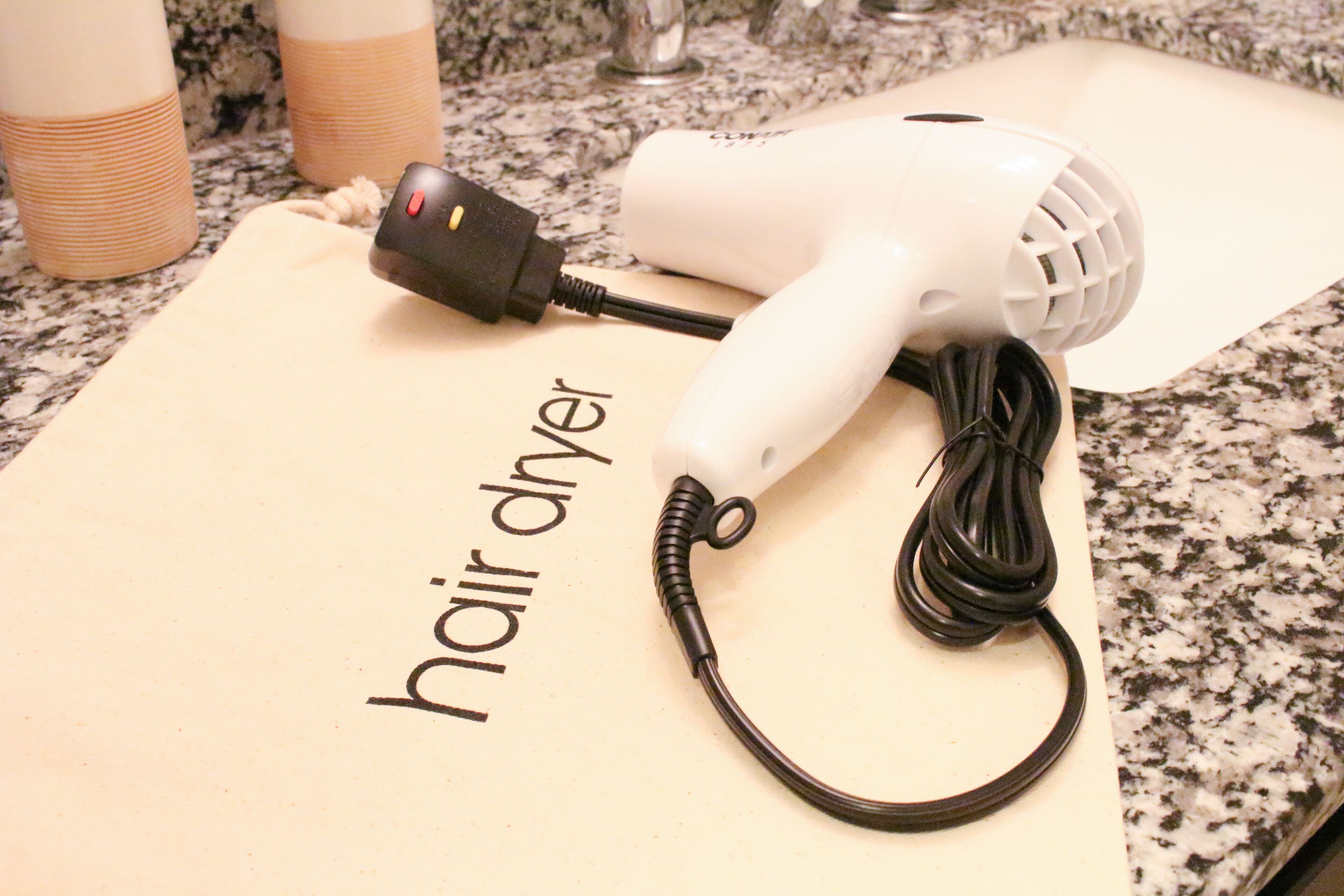 A hair dryer on a countertop with a piece of paper labeled "hair dryer" and two cups in the background.