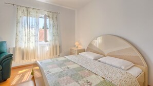 A bedroom with a bed, a nightstand, a lamp, a chair, and a window with curtains.