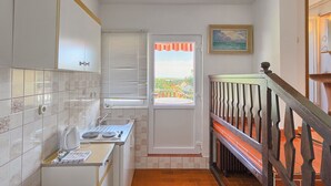 A narrow kitchen with a window, a door leading outside, and a staircase with a wooden railing.