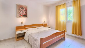 Ein Schlafzimmer mit einem Holzbett, Nachttischen, einem Tischchen, einem Bild an der Wand und einem Fenster mit Vorhängen.