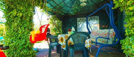 An outdoor seating area with a table and chairs, surrounded by greenery and a blue canopy.