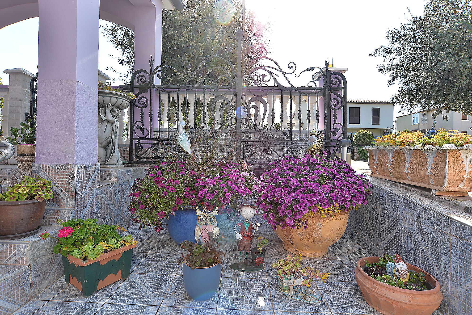 A courtyard with a decorative iron gate, potted plants, and a tiled floor.