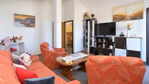 A living room with a sofa, chairs, a coffee table, a bookshelf, a television, and a painting on the wall.