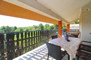 A covered outdoor seating area with a table and chairs, a brick pillar, and a view of greenery.