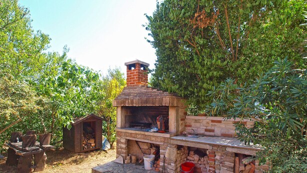 An outdoor brick-built barbecue area with a chimney, surrounded by trees and a small wooden structure. - Apartment 1224/11230 (Istria - Premantura), 300m from the beach (Premantura)