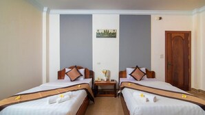 Una habitación de hotel con dos camas individuales, una mesita de noche pequeña con lámpara y una puerta de madera.