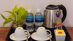 Una bandeja con dos tazas blancas, dos botellas de agua, una tetera, una caja de té Lipton y una pequeña planta en maceta.