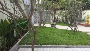 Un jardín con un árbol plantado en una jardinera cuadrada, rodeado de un patio empedrado.
