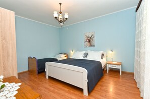 Une chambre à coucher avec un lit, deux tables de chevet, une commode, un plancher en bois, un lustre et un tableau au mur.