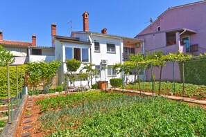 Un quartier résidentiel avec un jardin devant une maison blanche à toit rouge, entourée d’autres maisons.