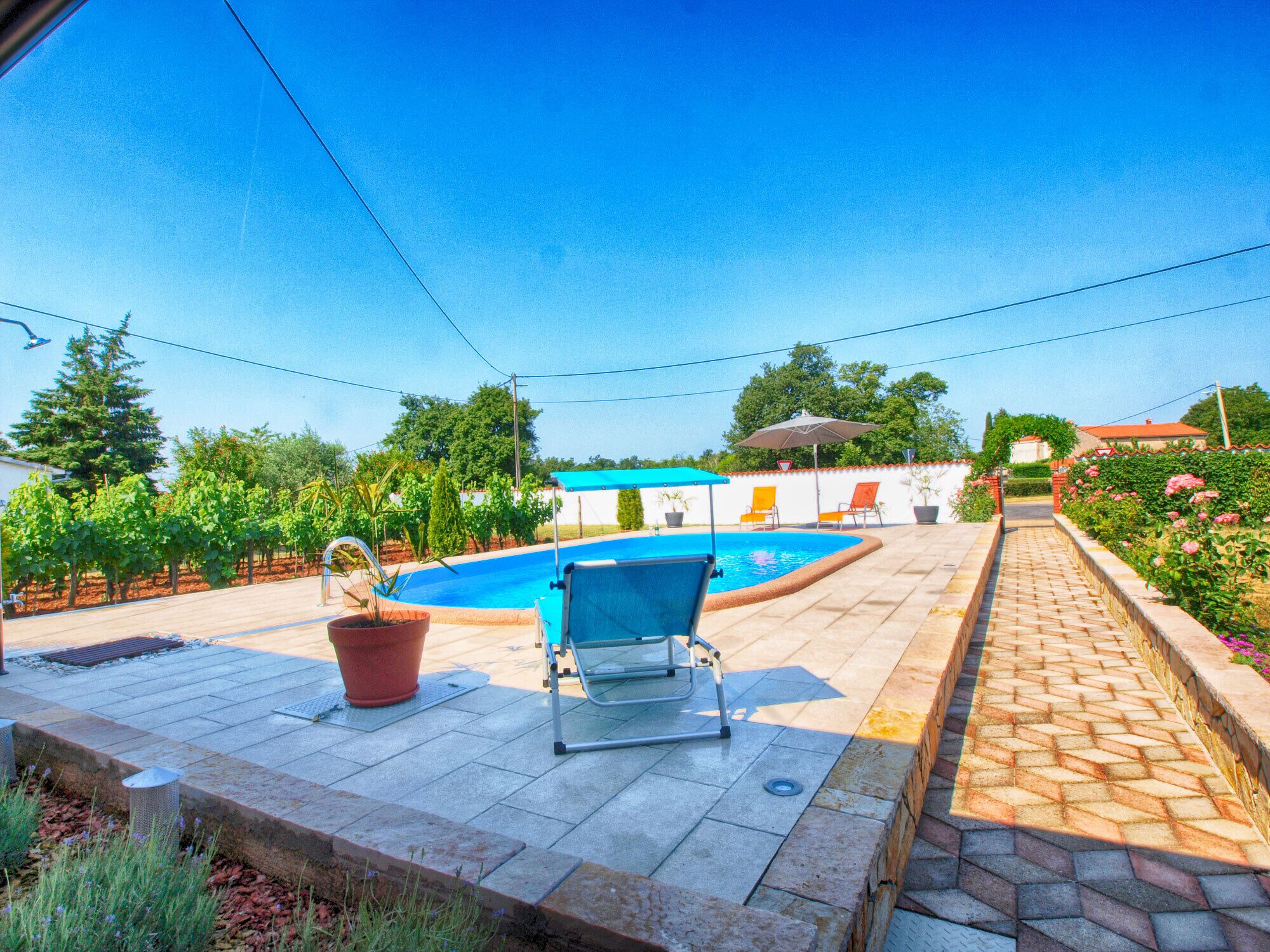 An outdoor swimming pool area with a blue chair, potted plants, and a tiled walkway.