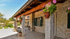 A stone building with a wooden pergola, potted flowers, and a stone floor.
