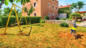 Um edifício residencial com fachada vermelha, baloiço e um pequeno jardim.