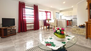 A modern living room with a flat-screen TV, a dining area with a table and chairs, and a kitchen with appliances. - Apartment 1251/11917 (Istria - Fažana), 350m from the beach (Fažana)