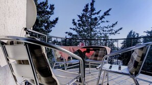 Ein Balkon mit Metallstühlen und einem Tisch, der auf einen bewaldeten Bereich blickt.