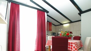 Ein Essbereich mit einem für zwei Personen gedeckten Tisch, roten Vorhängen und einer Küche im Hintergrund.
