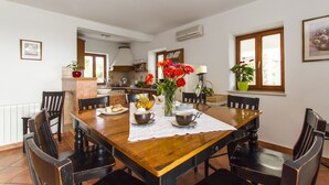 A dining area with a wooden table, chairs, and a vase of flowers. There is a kitchen in the background with a window and an air conditioning unit. - Villa 1254/11990 (Istria - Skitača), 5000m from the beach (Skitača)