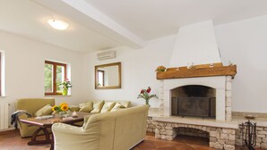 A living room with a stone fireplace, a sofa, a coffee table, and a window with plants. - Villa 1254/11990 (Istria - Skitača), 5000m from the beach (Skitača)