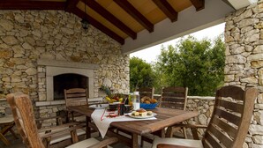 An outdoor patio with stone walls, a fireplace, wooden chairs, and a table set for a meal. - Villa 1254/11990 (Istria - Skitača), 5000m from the beach (Skitača)