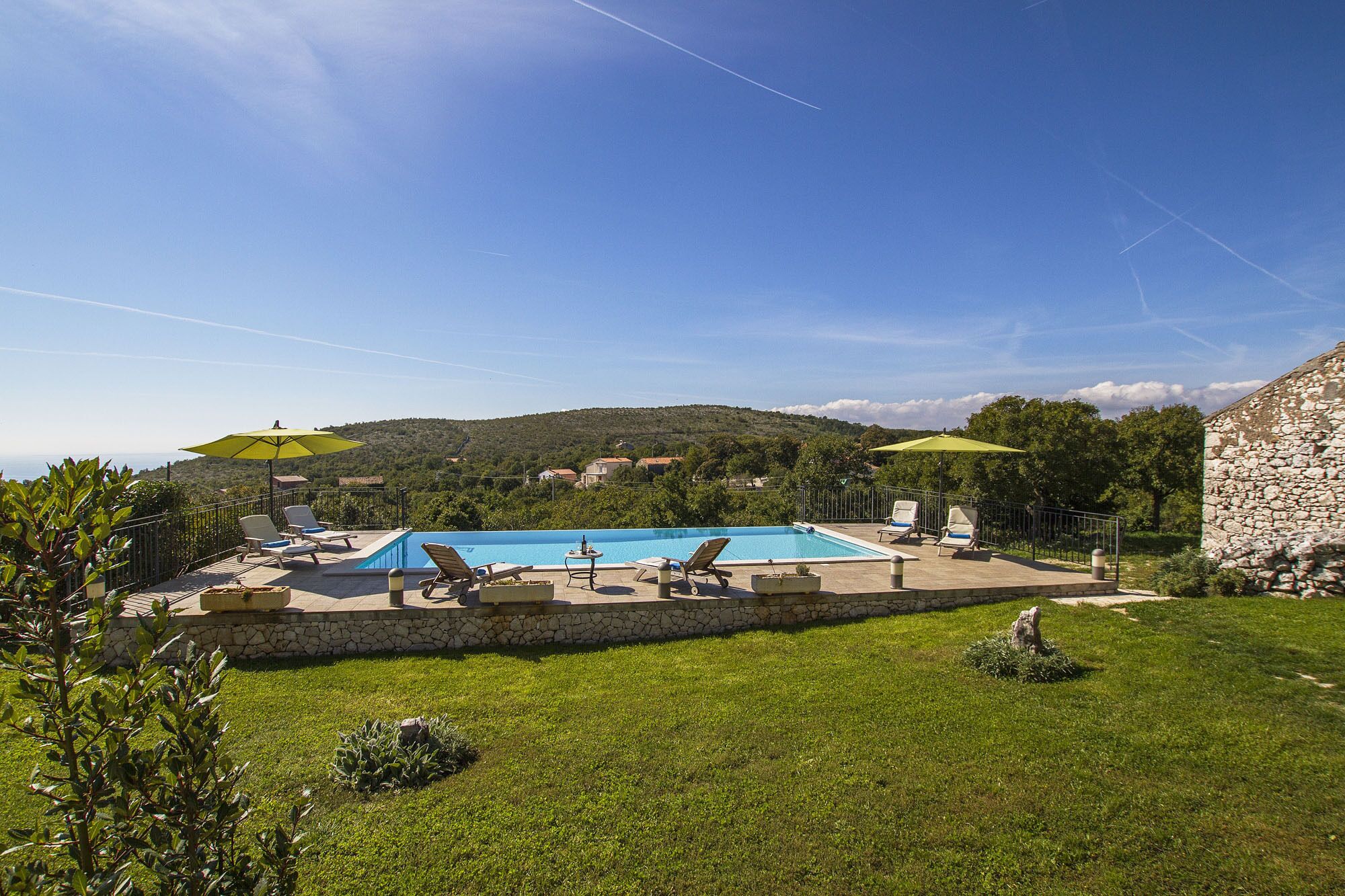 Un espace piscine agrémenté de chaises longues et de parasols, entouré d’un mur de pierre et de verdure.