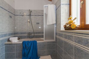 A bathroom with a bathtub, a shower, and a window with a basket of flowers.