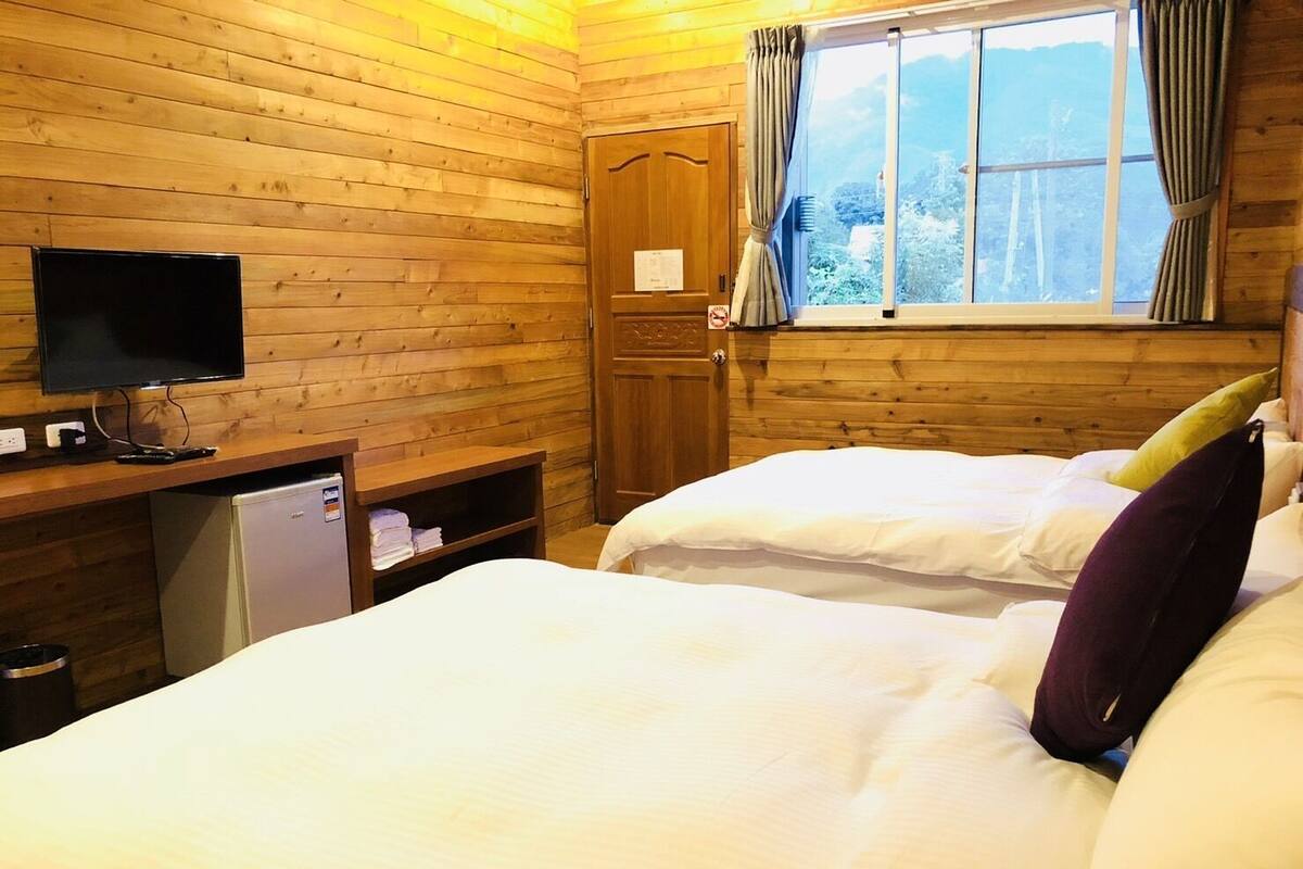 A wooden cabin room with two beds, a television, and a small refrigerator.