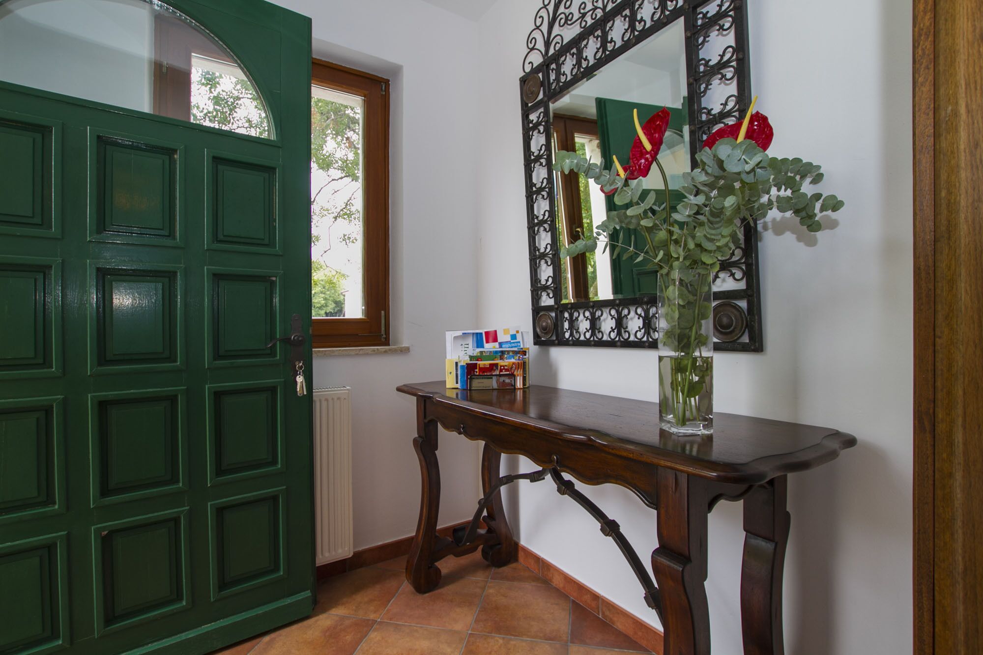 A green door, a wooden console table with a vase of flowers, and a mirror with a decorative frame.