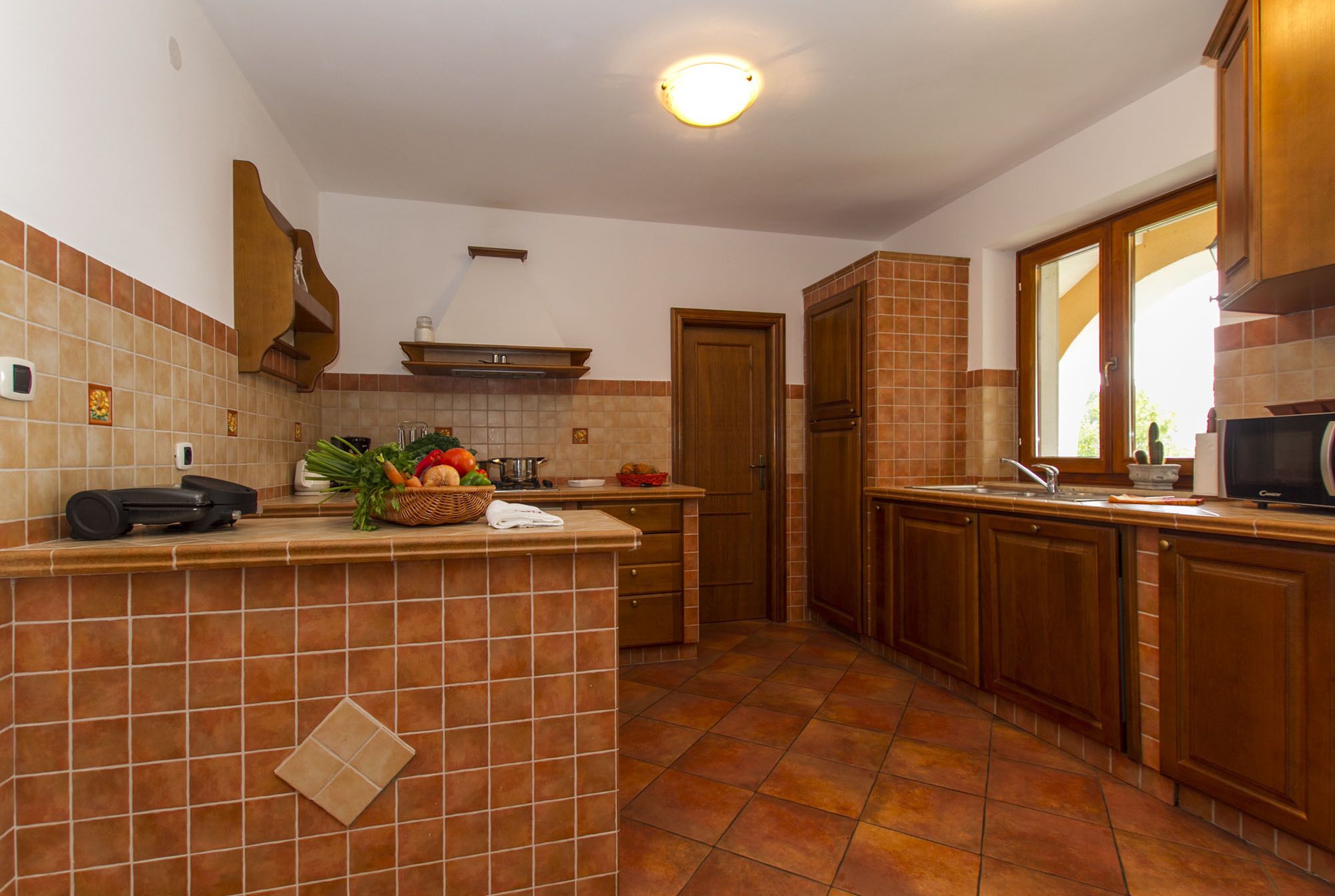Une cuisine avec un mur recouvert de carreaux, des meubles en bois, un îlot central où sont disposés des produits frais et un four à micro-ondes posé sur le plan de travail.