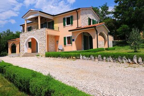 A two-story house with a stone facade, green shutters, and a gravel driveway.
